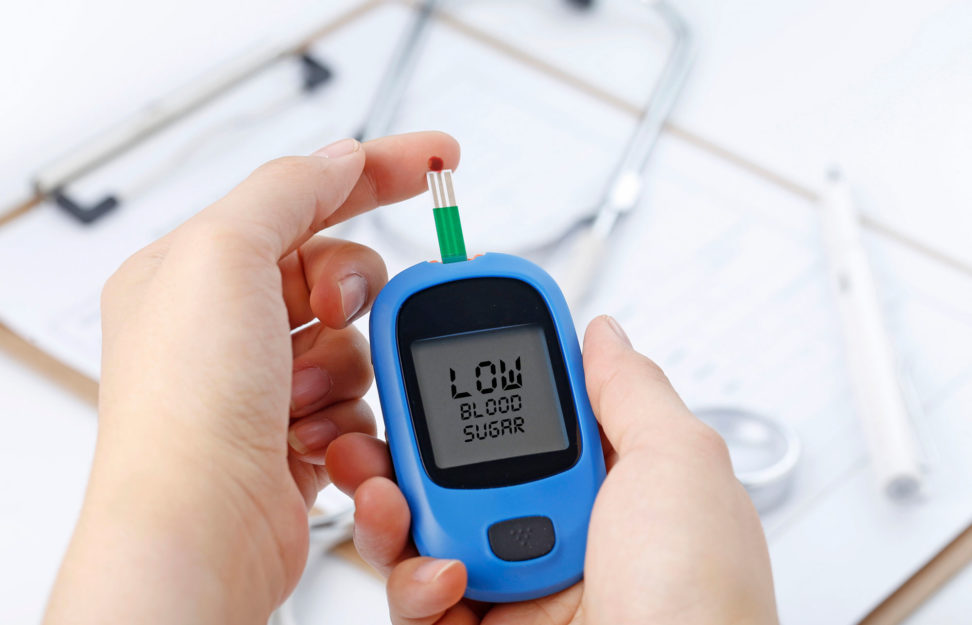 hand-holding-blood-glucose-meter-measuring-blood-sugar-background-is-stethoscope-chart-file-2-972x625